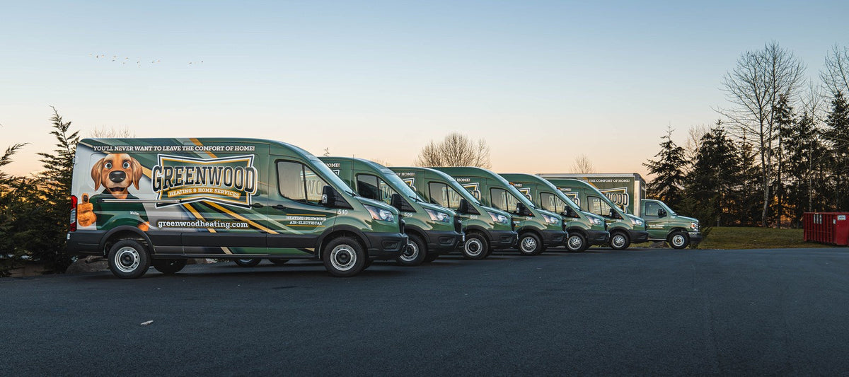Lead Ford Transit van in a green Greenwood Heating & Home Services wrap with dog mascot, followed by matching fleet vans