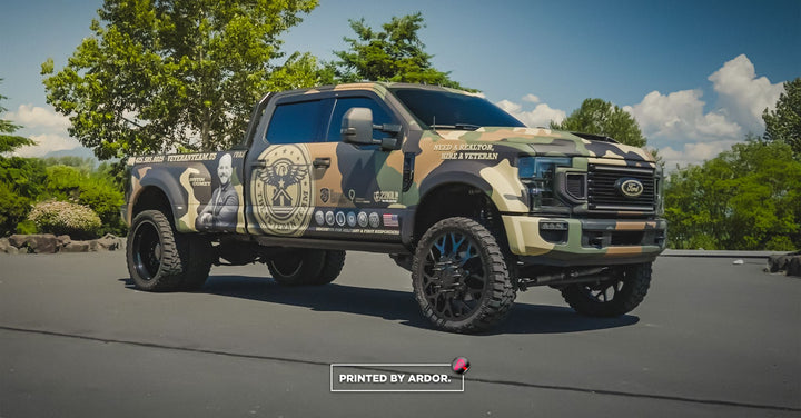 Lifted Ford Super Duty dually with a woodland camo printed wrap and veteran realtor graphics