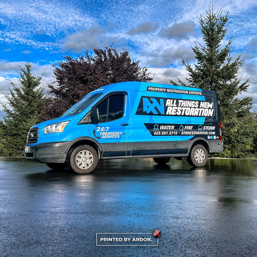 Custom-wrapped van for All Things New Restoration, offering water, fire, and storm damage services, with 24/7 emergency contact information.