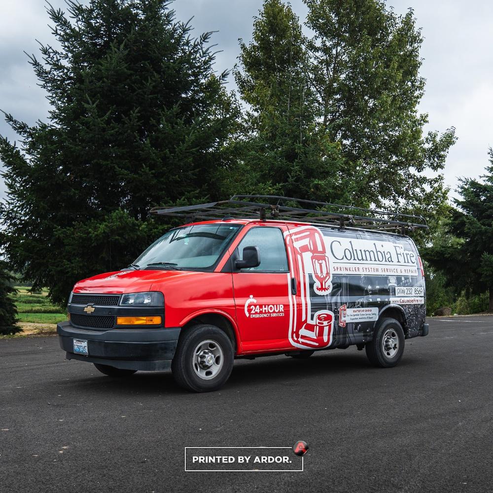 Columbia Fire van with a red and black wrap, advertising sprinkler system service and repair with 24-hour emergency contact info, parked outdoors.