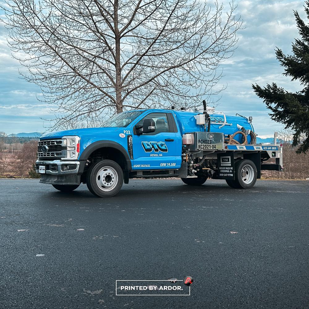DTG Recycle truck wrapped in bright blue with company branding and service details, parked on a road near trees and a clear sky.