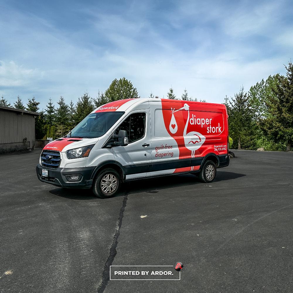 Diaper Stork van with a bold red and white wrap, displaying company branding, stork logo, and contact information, parked on a clear day.