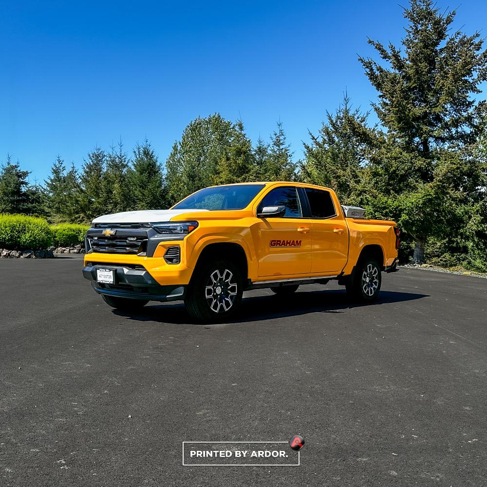 A Chevrolet Colorado wrapped in yellow with Graham Construction branding, showcasing the company logo on the doors, parked outdoors.