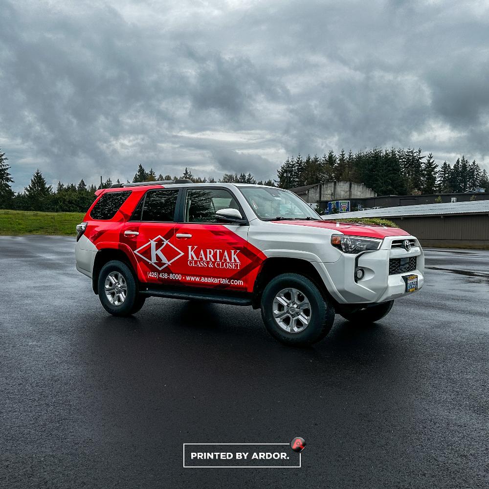 Kartak Glass & Closet SUV with a red and white custom wrap, displaying company logo, contact information, and website, parked on a wet road.