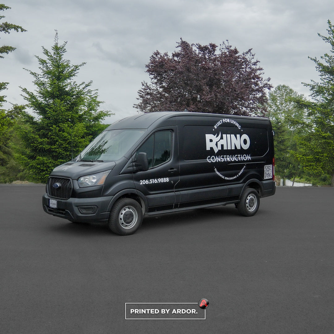 Rhino Construction van with a sleek black wrap, featuring bold white lettering, company phone number, and QR code, parked on a paved road.