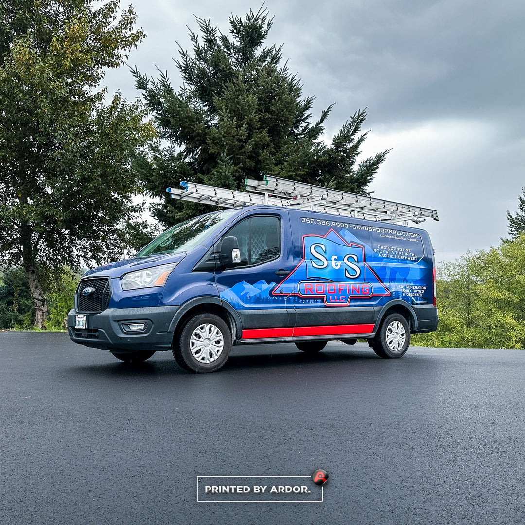 S&S Roofing van with custom wrap featuring blue mountains and red highlights, parked near trees with company website and phone number displayed.