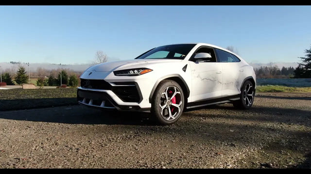 White Lamborghini Urus in a printed marble wrap with red brake calipers, parked on gravel on a sunny day