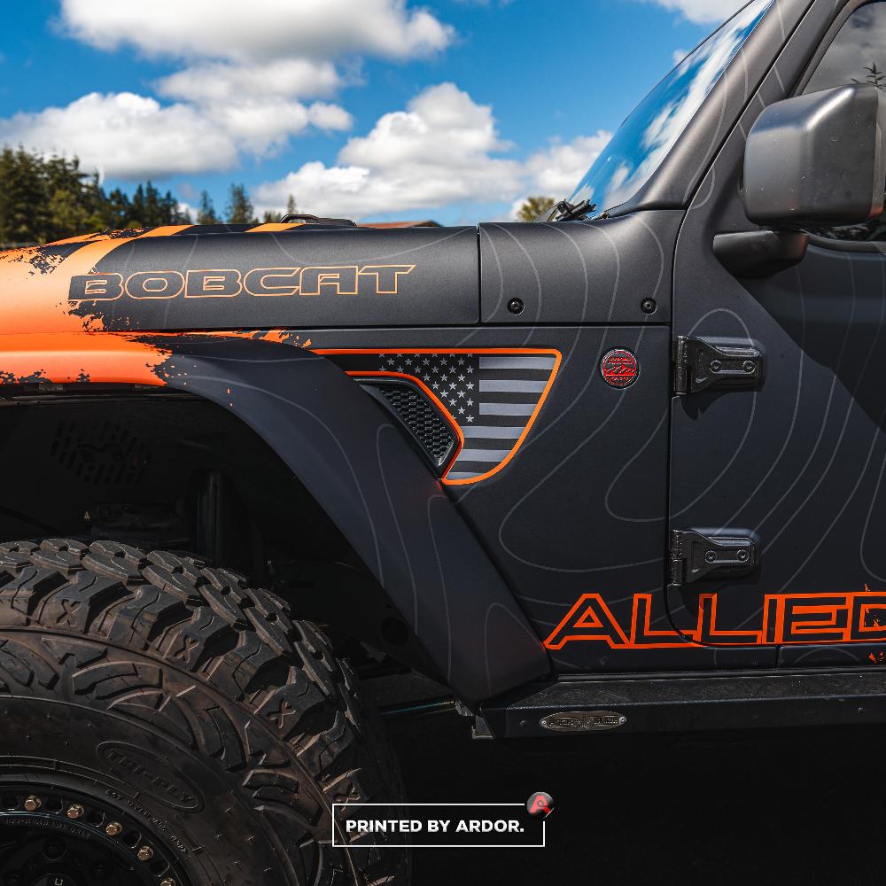 Close-up of a custom-wrapped Allied Motorsport Jeep with 'BOBCAT' branding and an American flag design on the fender, showing rugged off-road tires.