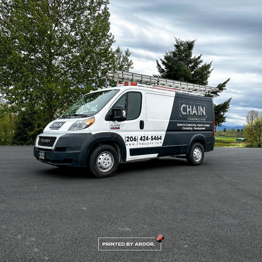 Chain Construction Ram ProMaster van with a black and white wrap and ladders on the roof rack