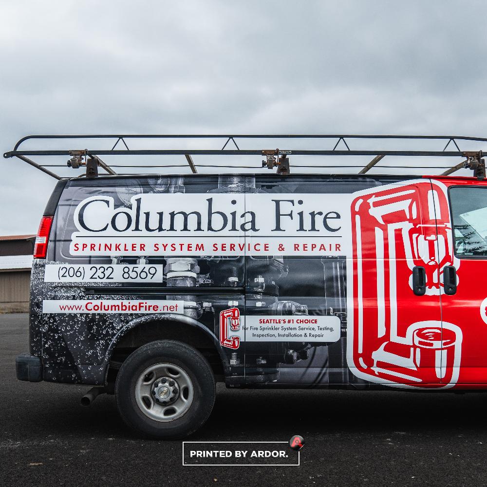 Close-up view of Columbia Fire van wrap displaying bold text promoting sprinkler system service, repair, and emergency contact info.