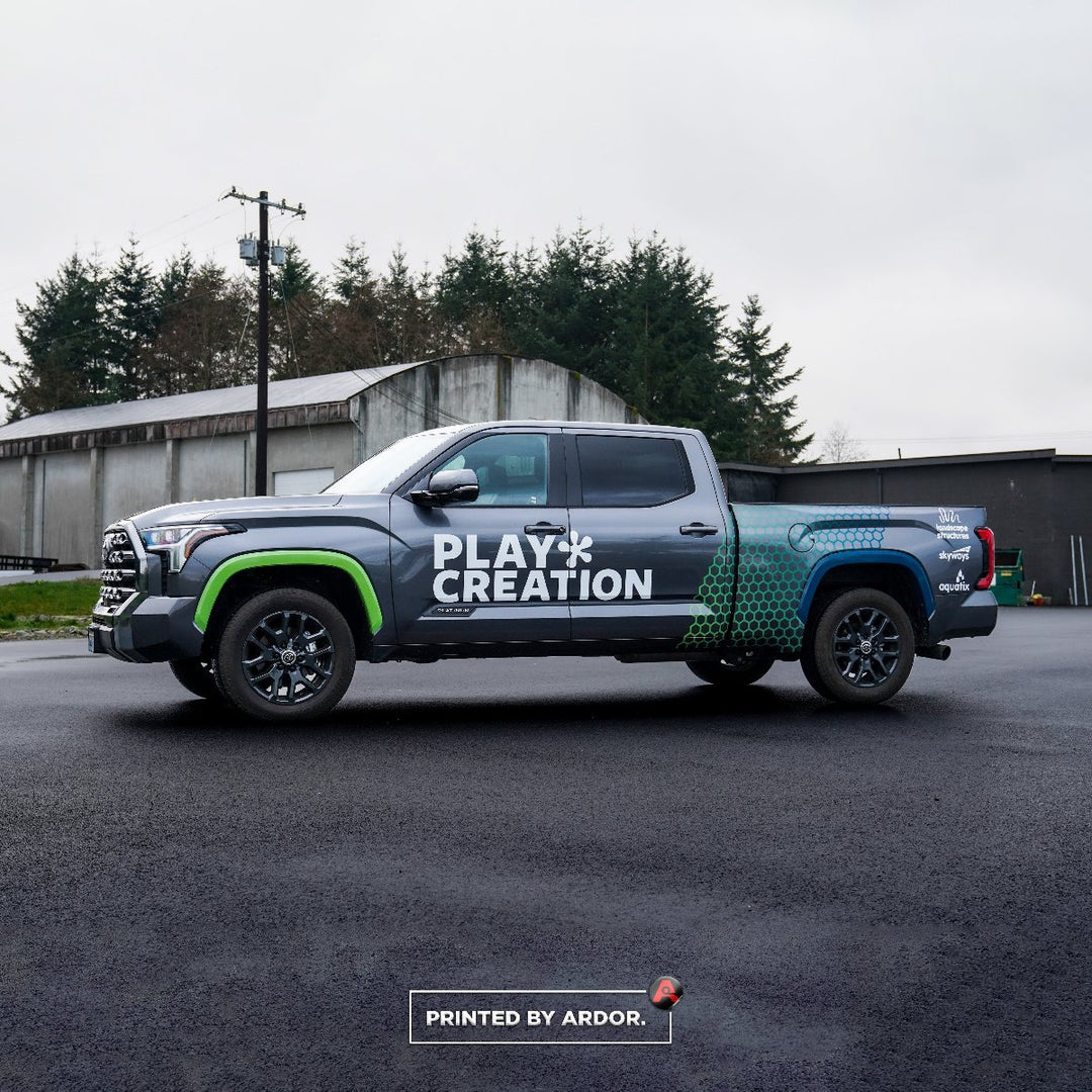 A grey Toyota Truck with Play Creation vinyl lettering across the doors and a half wrap on the bed sides.