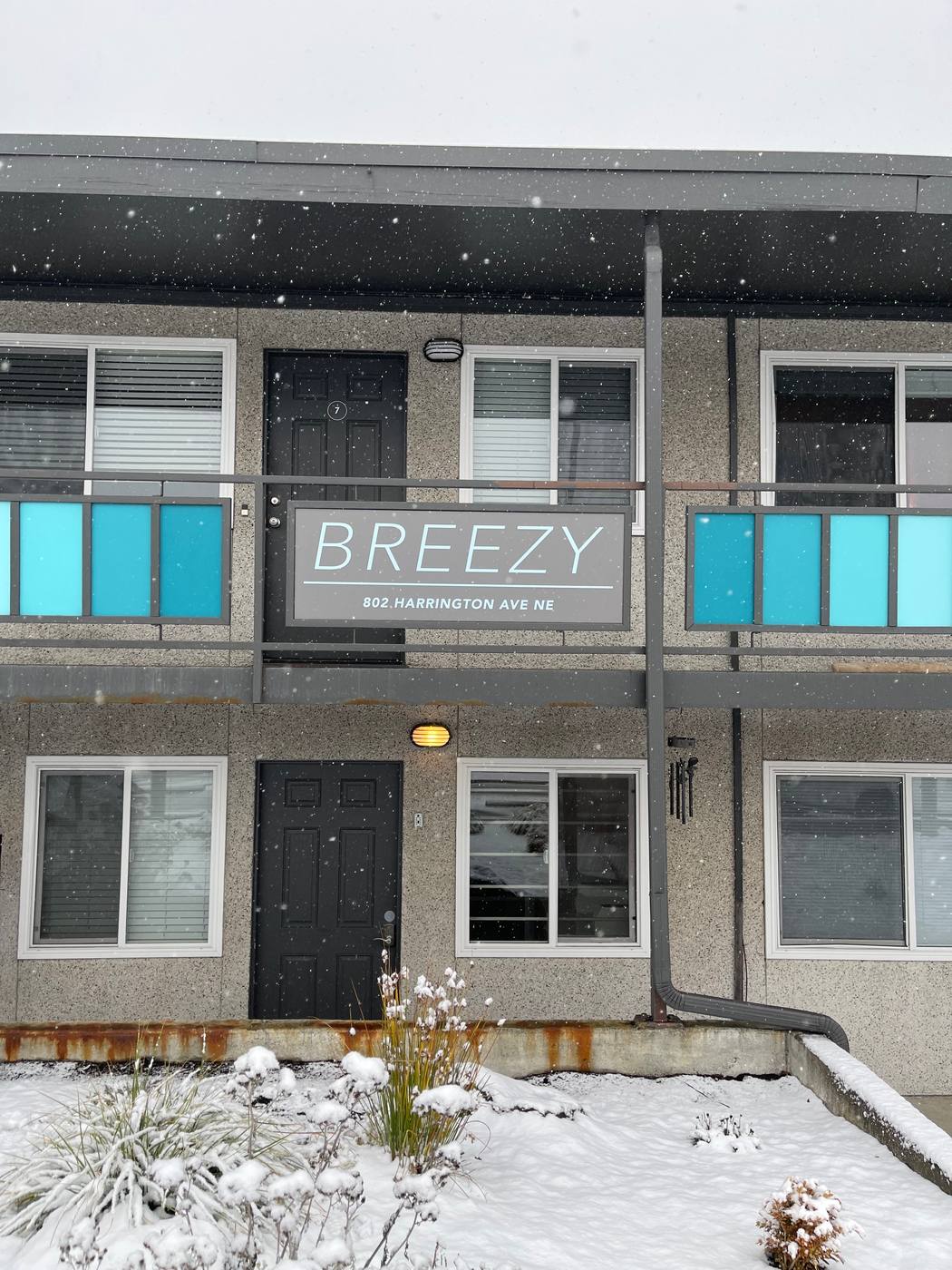 Gray Breezy apartment sign with street address mounted between the floors of a two-story building in the snow