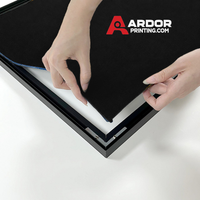 Hands pressing the silicone edge of the fabric graphic into the black Wall Mount SEG frame, Ardor Printing branding