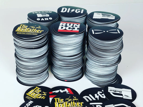 Three stacks of black and white DigiTrak circle stickers with loose Run DCI and The Rodfather stickers in front