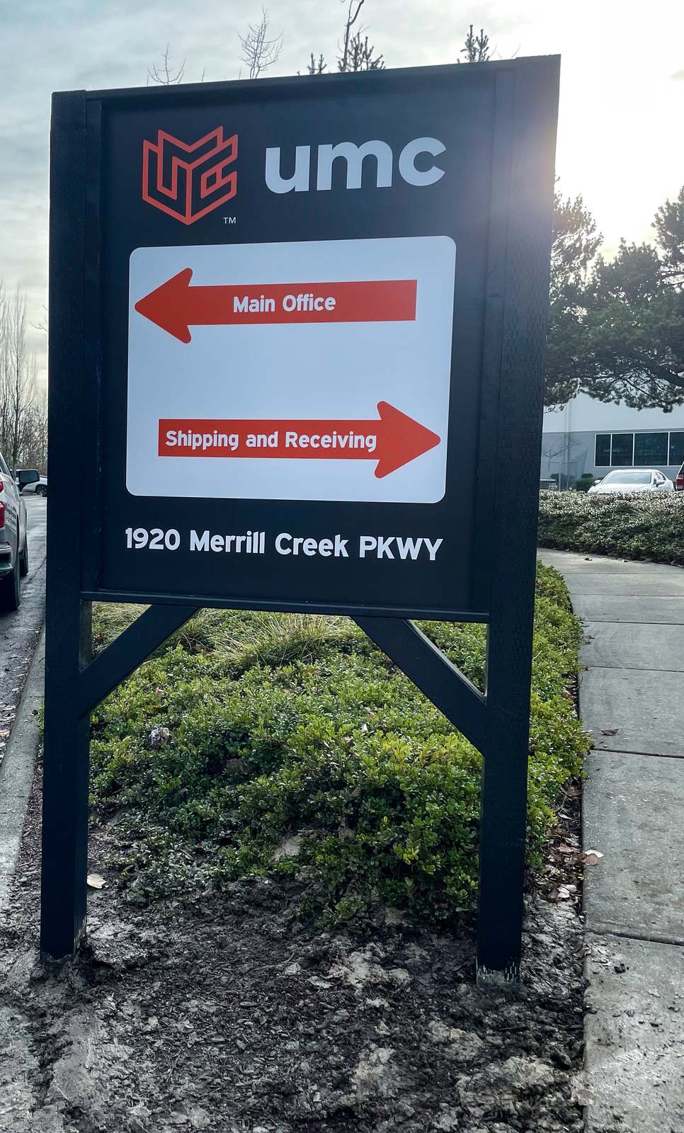 Black post-and-panel UMC sign with arrows to Main Office and Shipping and Receiving in Everett, WA